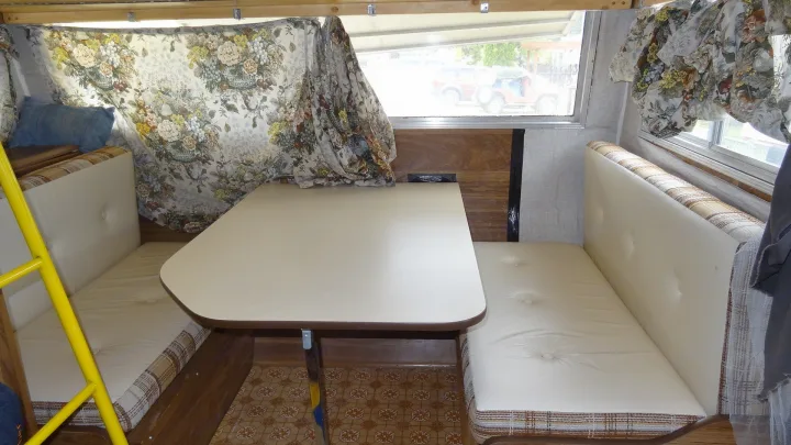 RV rental dining space: interior view with a table, cream cushioned benches, and floral curtains. Ideal for camper travel.. Vintage Trailers Skylark 180 1979