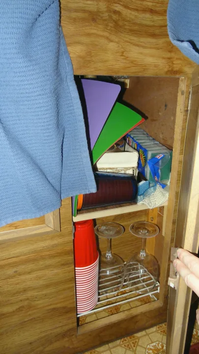 RV rental cabinet: Compact kitchen storage with red cups, wine glasses, sponges, and cutting boards.. Vintage Trailers Skylark 180 1979