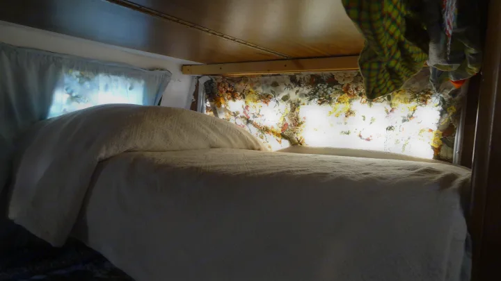 Cozy RV rental bed with white bedding, floral curtains, & bright window light. Perfect for travel comfort.. Vintage Trailers Skylark 180 1979