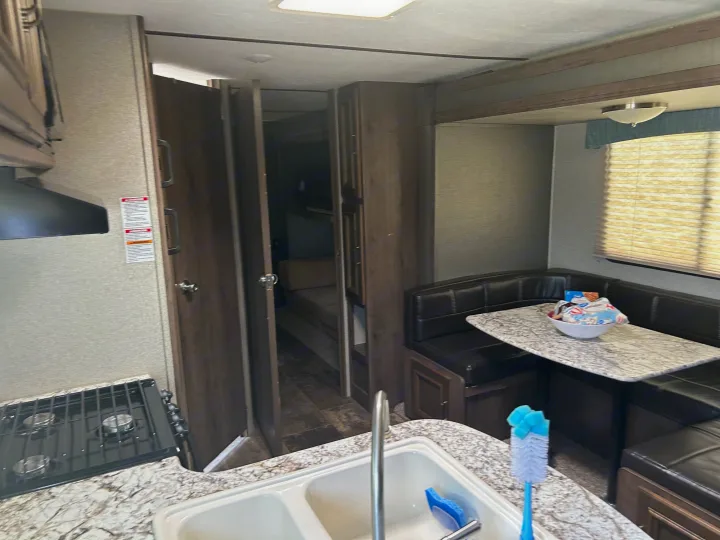 View inside an RV rental showing a kitchen with stove and double sink, next to a comfortable dining booth area.. Keystone RV Passport Grand Touring 2018