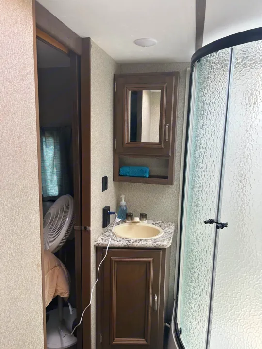 RV rental bathroom featuring a sink, medicine cabinet, curved glass shower, and a fan visible in the adjacent room.. Keystone RV Passport Grand Touring 2018