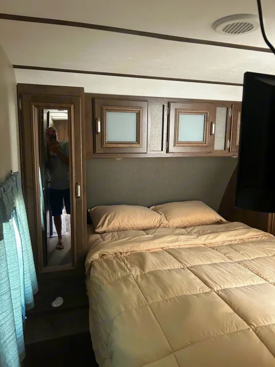 Comfortable RV rental bedroom featuring a cozy bed, overhead cabinets, and a full-length mirror.. Keystone RV Passport Grand Touring 2018