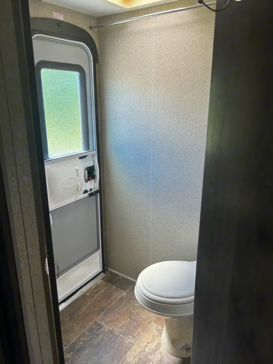 Compact RV rental interior showing an exit door with screen on the left and a toilet on the right. Functional for travel.. Keystone RV Passport Grand Touring 2018