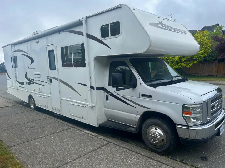 Large white **RV rental** motorhome with brown graphics, parked on a street curb. Shows its full side profile.. Adventurer Adventurer Motorhome 2012