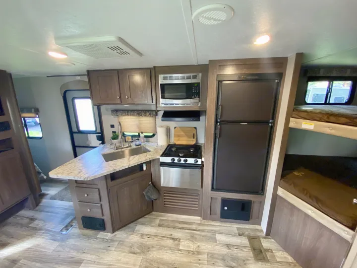 RV rental interior: kitchen with stove, microwave, fridge, light wood cabinets & flooring, plus bunk beds.. Keystone RV Hideout 2018
