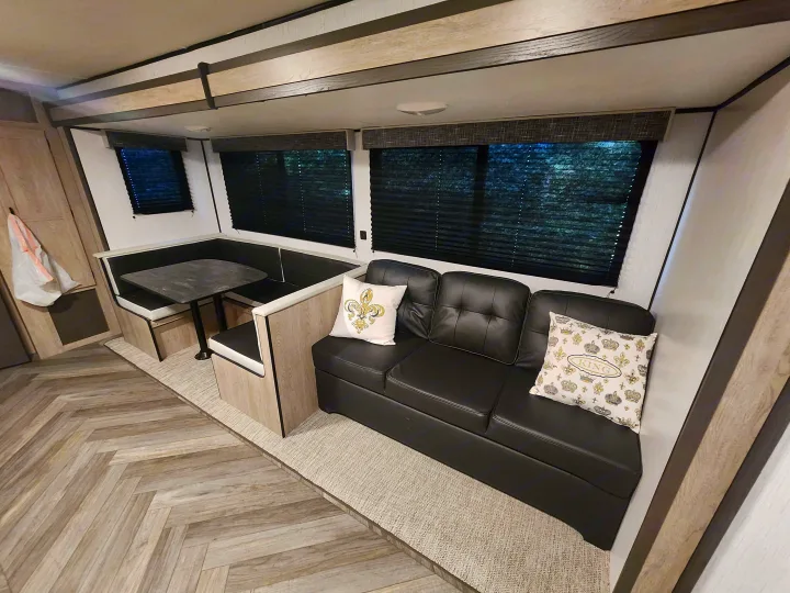 RV rental interior: A bright, modern living area with black sofa, U-shaped dinette, and wood-look flooring over a rug.. Heartland RVs Prowler 2022