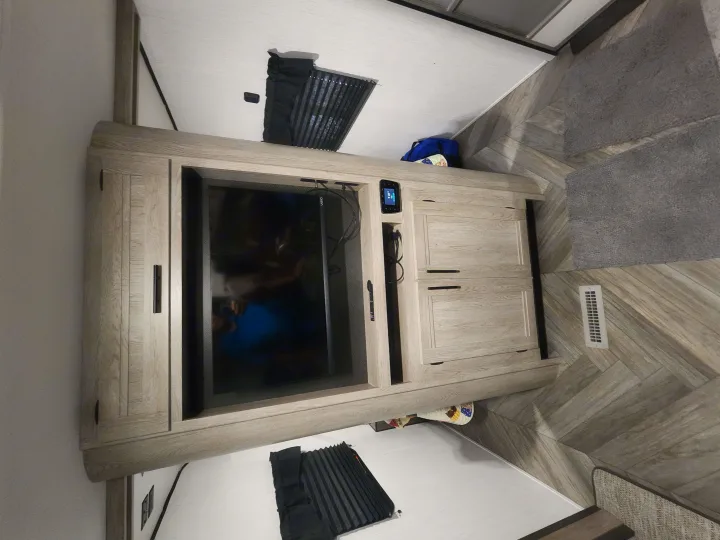 Inside an RV rental: a cozy living area with light wood cabinets, a built-in TV, and a stylish herringbone floor.. Heartland RVs Prowler 2022