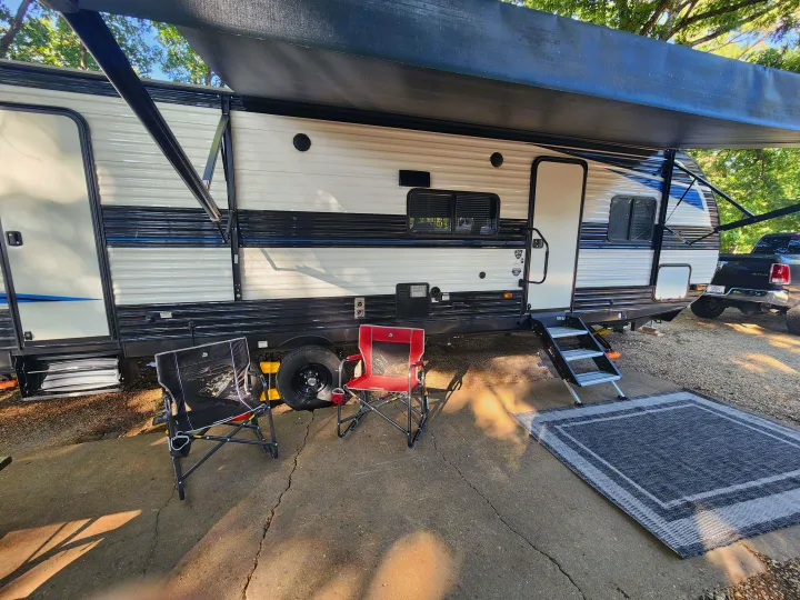 Relaxing RV rental campsite setup: extended awning, two chairs, and an outdoor rug on concrete. Perfect for glamping!. Heartland RVs Prowler 2022