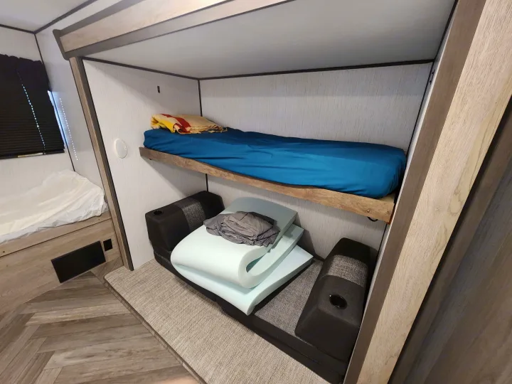 RV rental interior featuring comfortable bunk beds with a blue mattress and a lower lounge area with foam cushions.. Heartland RVs Prowler 2022
