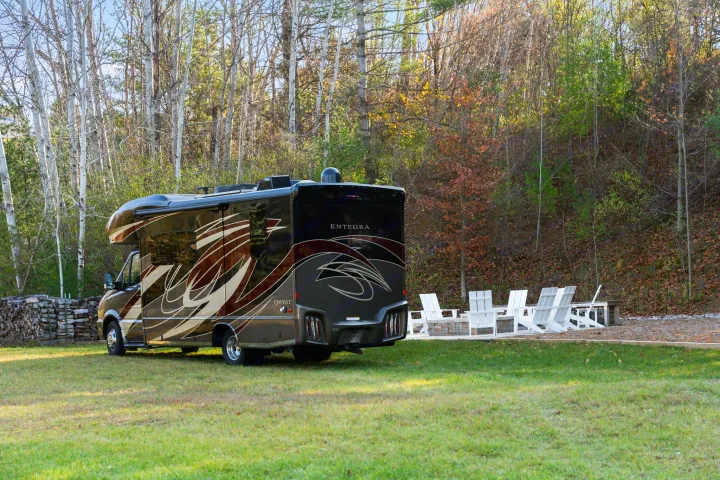 This sleek Entegra Qwest RV rental is parked on a grassy lawn, with a fire pit and white chairs ready for a cozy evening by the woods.. Entegra Coach Qwest 2018