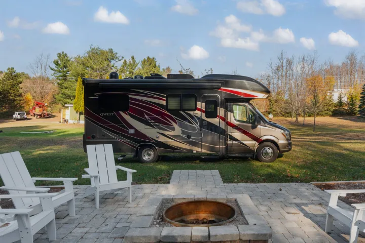 Enjoy your RV rental: a modern motorhome parked beside a cozy patio with a fire pit and white chairs.. Entegra Coach Qwest 2018
