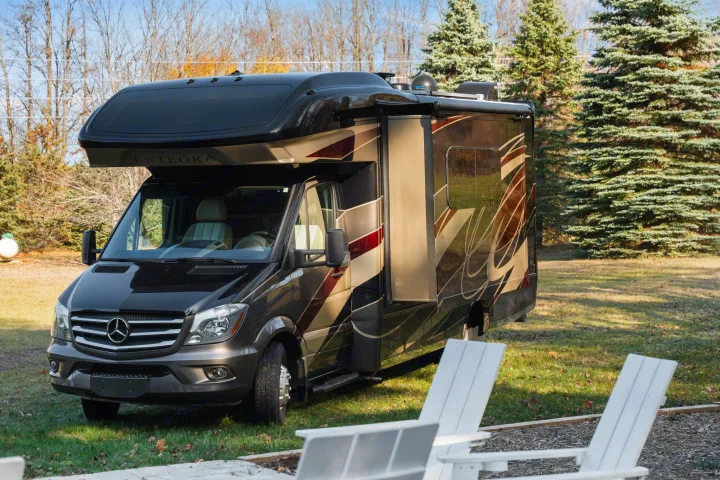 Luxury Entegra Class C RV rental, a black & brown Mercedes-Benz motorhome on grass, with white chairs in foreground.. Entegra Coach Qwest 2018