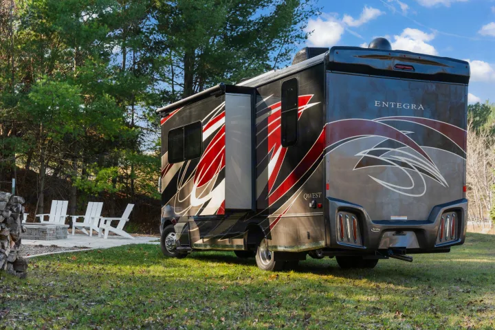 A sleek black/red Entegra Qwest RV rental, with slide-out extended, parked on green grass near a fire pit area with chairs.. Entegra Coach Qwest 2018