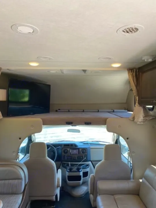 Interior of a modern RV rental, showing the front cockpit, an overhead bunk bed, and comfortable seating areas.. Thor Chateau 2017