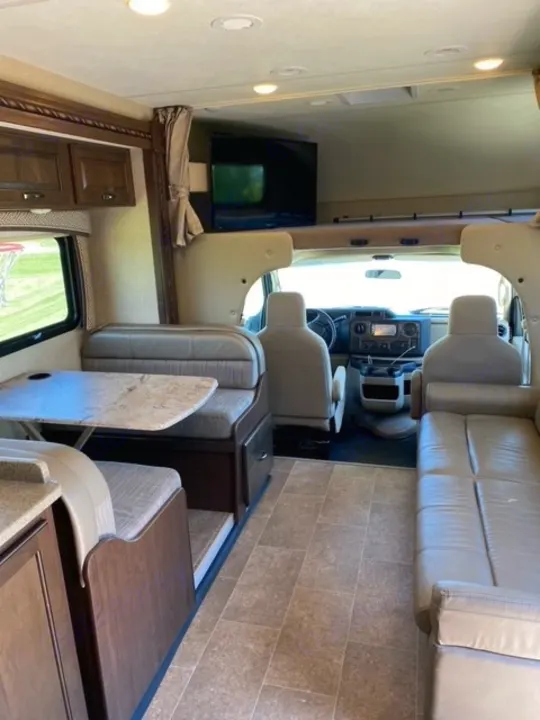 Spacious RV rental interior with dinette, sofa, overhead bunk, TV, and front cockpit area. Ideal for comfortable road trips.. Thor Chateau 2017