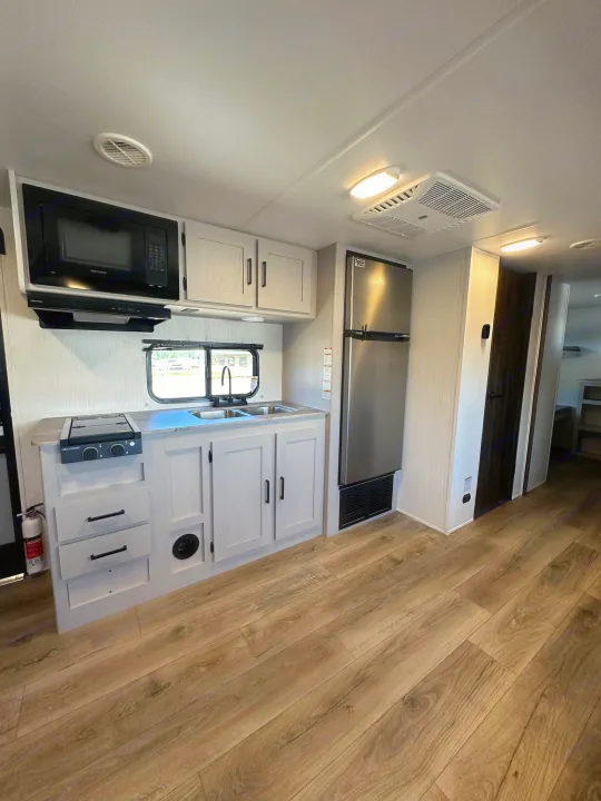 Bright RV rental kitchen with light wood-look flooring, modern appliances, and ample storage for comfortable travel.. Heartland Prowler Lynx 302BHX 2025