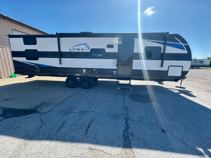 Bright white & black Lynx travel trailer, an excellent RV rental option. Sunny outdoor view shows blue accents & multiple windows.. Heartland Prowler Lynx 302BHX 2025