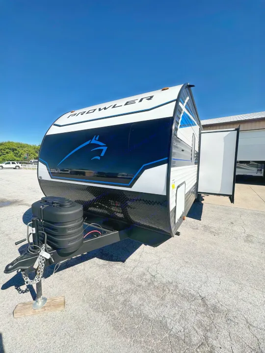 White and black Prowler travel trailer, great for rv rental, parked under a clear blue sky. Open door on side.. Heartland Prowler Lynx 302BHX 2025