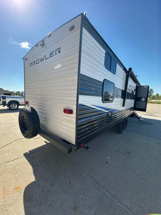 This Prowler Lynx travel trailer, ideal for an RV rental, features a white exterior with black and blue accents, an open entry door, and a rear-mounted spare tire.. Heartland Prowler Lynx 302BHX 2025