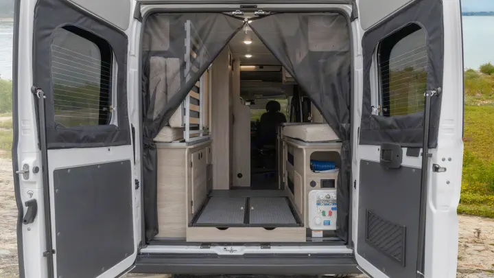 RV rental rear view: Open doors reveal a camper van interior with mesh screen, modular bed, storage, and utility panel.. Winnebago Solis 2021