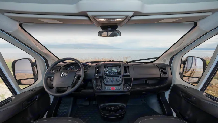 RV rental: Inside a camper van's cockpit, showing the dashboard, steering wheel, and a scenic waterfront view ahead.. Winnebago Solis 2021