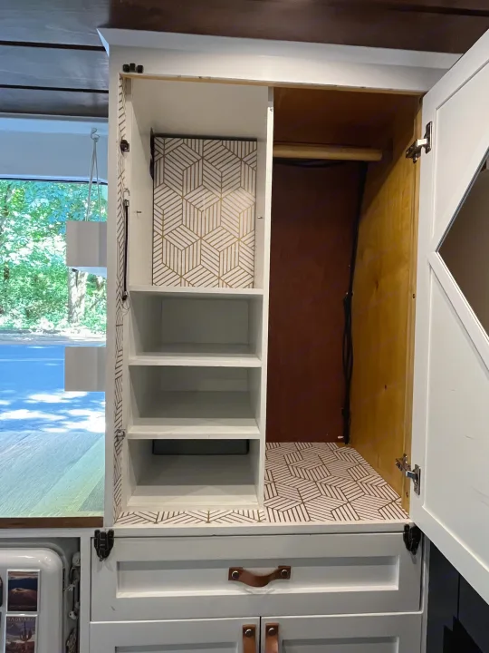 Spacious white wardrobe in an RV rental, featuring geometric patterned lining, shelves, and a hanging rod.. Dodge Sprinter 2018