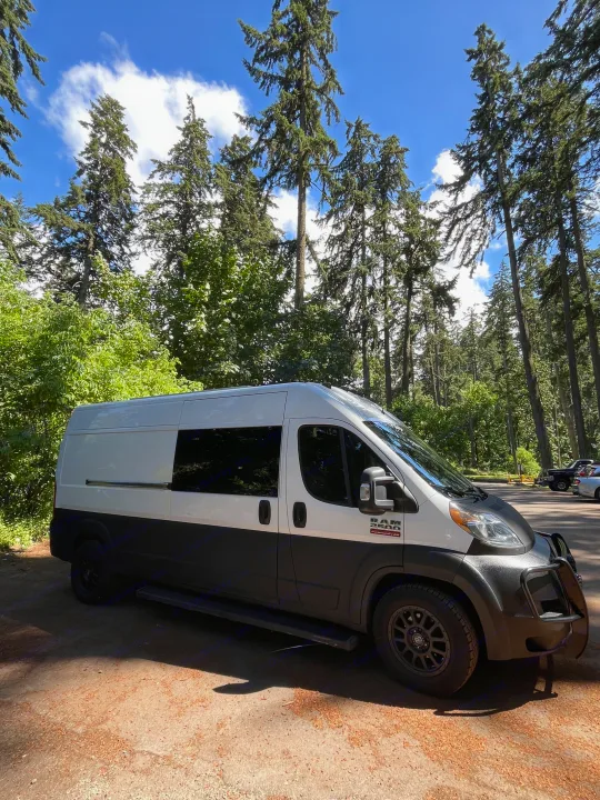 Ram ProMaster camper van, an ideal RV rental parked amidst tall forest trees. Ready for your next outdoor adventure!. Dodge Sprinter 2018
