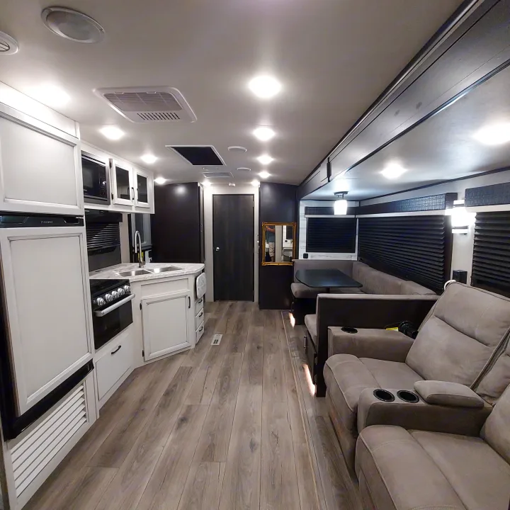 Bright, modern rv rental interior features a kitchen, dining booth, and comfortable reclining living area with wood-look floors.. Jayco White Hawk 2021