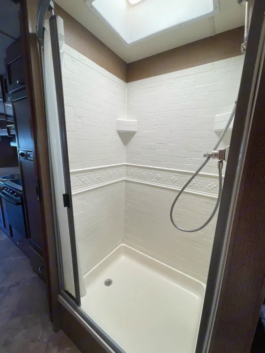 Clean RV rental shower with white tiled walls, compact base, skylight, and handheld showerhead visible inside.. Thor Motor Coach A.C.E 2017