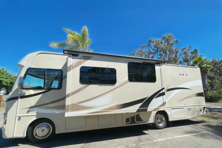 Beige and brown ACE motorhome, an RV rental, parked outdoors under a clear blue sky. Details include its side, windows, and storage.. Thor Motor Coach A.C.E 2017