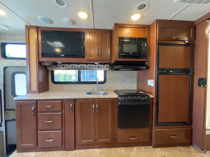 Well-equipped RV rental kitchen: sink, stove, microwave, refrigerator, and TV. Perfect for cooking and entertainment on the go.. Thor Motor Coach A.C.E 2017