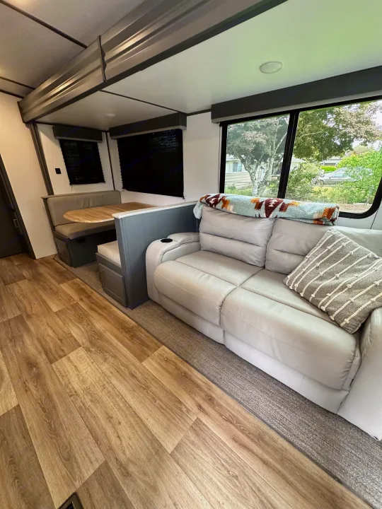 Modern RV rental interior: spacious living area with sofa, dinette, wood flooring, and large windows.. Keystone RV Bullet Ultra Lite 2022