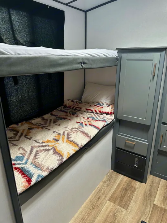 Inside an RV rental, two bunk beds are shown, ready for travelers. The lower bunk features a colorful patterned blanket.. Keystone RV Bullet Ultra Lite 2022