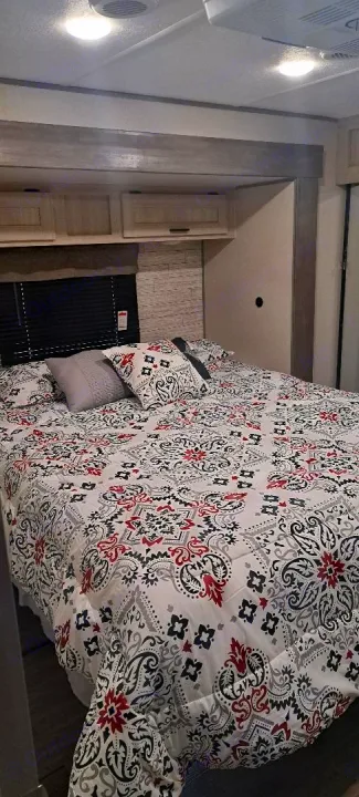 RV rental bedroom: a comfortable bed with a white, red, black, and grey patterned comforter and pillows.. Forest River Aurora Aurora 2024