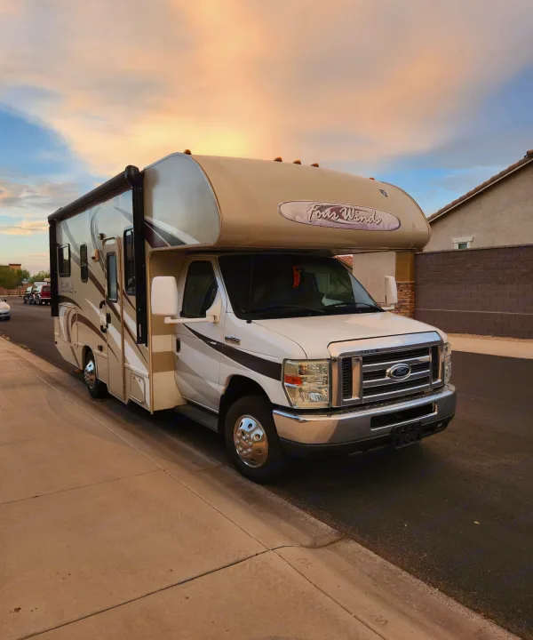 This Class C Four Winds RV rental, in white and tan, is parked curbside under a vibrant, colorful sky.. Thor Four Winds 2017