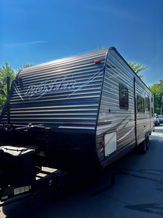 A grey Pioneer travel trailer RV, ideal for an RV rental, is seen parked outdoors on a sunny day.. Heartland RVs Pioneer 2018