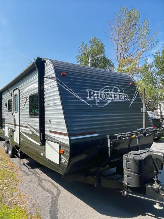 A grey and black Pioneer travel trailer (RV) with an awning, parked outdoors. Ready for your next RV rental adventure.. Heartland RVs Pioneer 2018