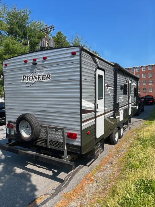 Rear and side of a grey and green Pioneer travel trailer, perfect for an RV rental. Features a rear spare tire and side door.. Heartland RVs Pioneer 2018