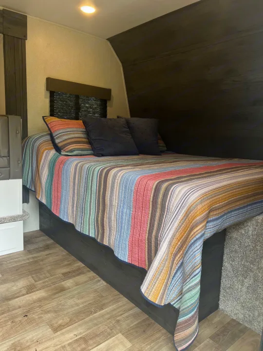Cozy rv rental bedroom featuring a colorful striped bed quilt, dark wood accents, and light flooring.. Keystone RV Hideout 2022