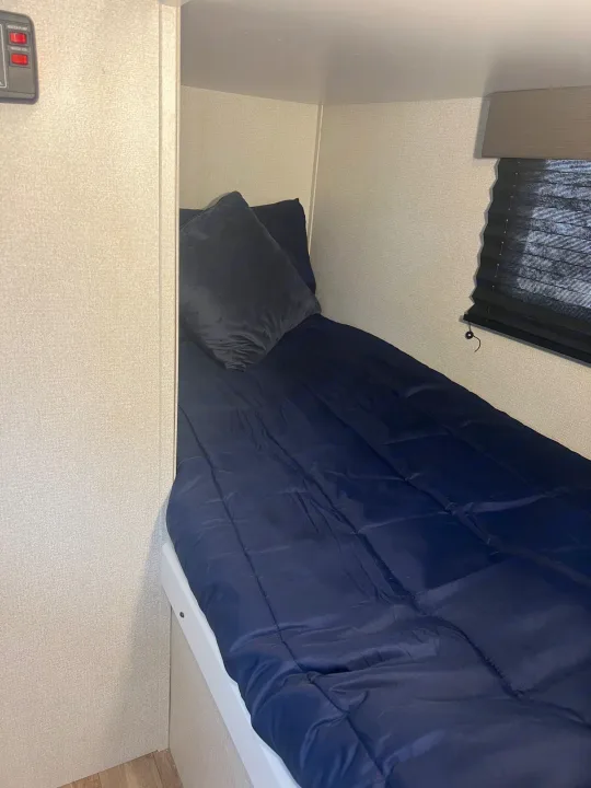 RV rental compact bunk bed setup with controls nearby, blue bedding, and a window blind.. Keystone RV Hideout 2022