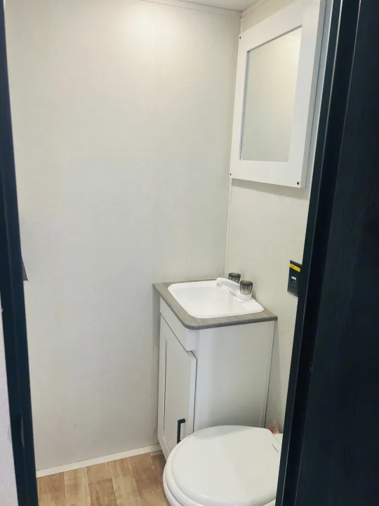 Compact bathroom in an RV rental with a sink, vanity, mirror, and toilet. Features wood-look floor and light walls.. Keystone RV Hideout 2022