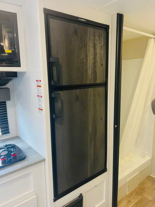 RV rental: Compact kitchen with Dometic fridge, microwave, stovetop, and adjacent shower/tub.. Keystone RV Hideout 2022