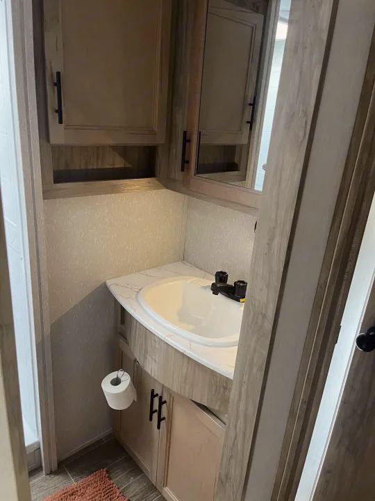 Compact RV rental bathroom with sink, mirror, and cabinetry. Includes a shower stall and toilet paper holder.. Forest River Cherokee Arctic Wolf 2021