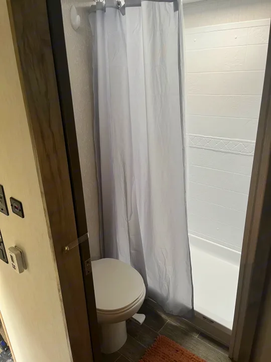 Inside an RV rental: a compact bathroom featuring a toilet, shower with curtain, and dark wood-look floor.. Forest River Cherokee Arctic Wolf 2021