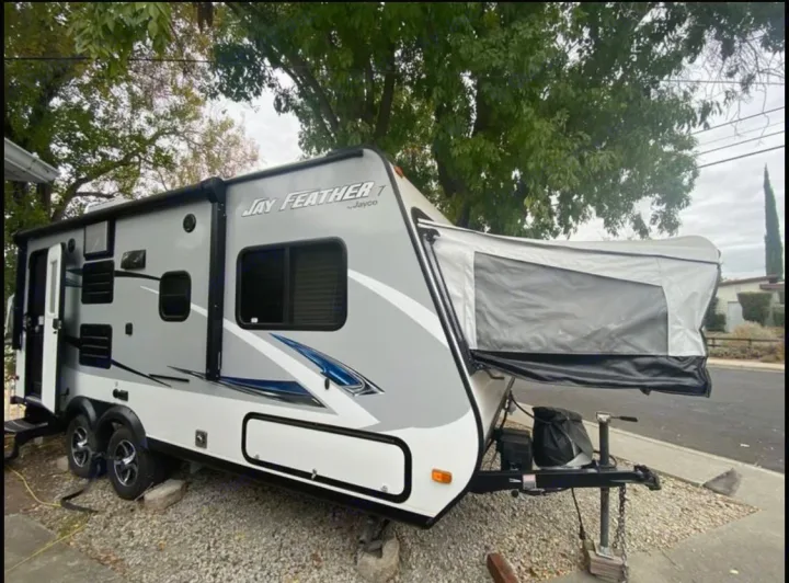 This grey & white Jayco Jay Feather T hybrid travel trailer, with its extended front bunk visible, is an ideal rv rental for outdoor adventures.. Jayco Jay Feather 2017