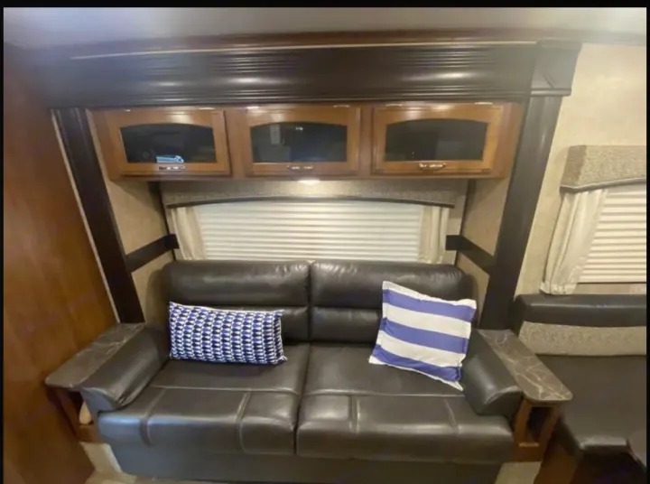 Cozy RV rental interior: dark leather sofa, decorative pillows, overhead cabinets, and window. Ideal for travel.. Jayco Jay Feather 2017