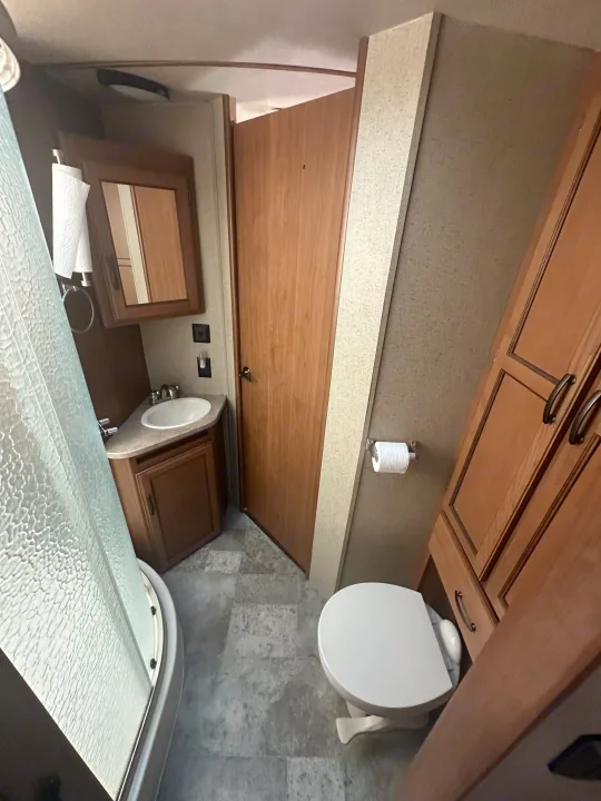 RV rental bathroom featuring a shower, sink vanity, toilet, and built-in wooden storage cabinets.. Crossroads RV Sunset Trail Super Lite 2017