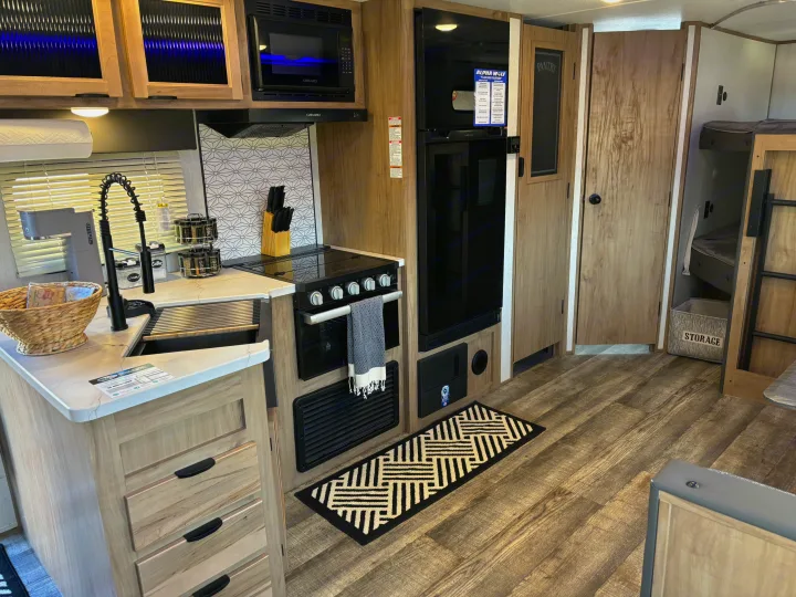 Inside this **rv rental**, discover a full kitchen with microwave, stove, sink, fridge, and nearby bunk beds.. Forest River ALPHA WOLF 26DBH-L 2024