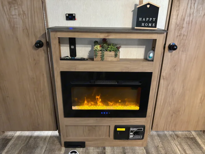 Comfortable RV rental interior featuring an electric fireplace with faux flames, built-in shelving, and a convenient RoadVac system.. Forest River ALPHA WOLF 26DBH-L 2024