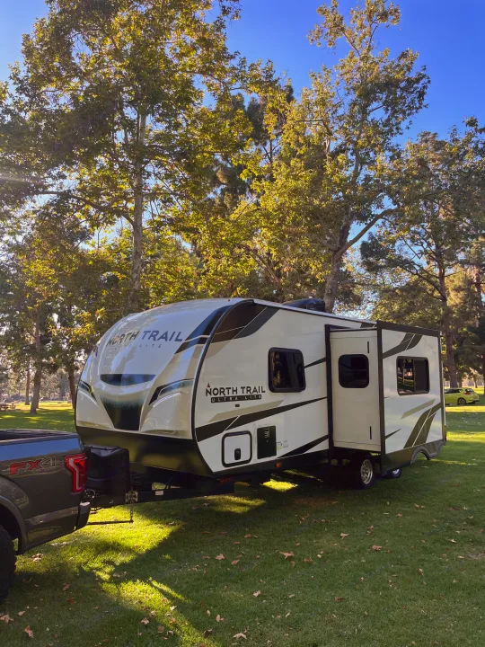 North Trail travel trailer hitched to a truck, ready for your next rv rental adventure in a lush park.. Heartland RVs North Trail 2022